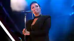 Demi Lovato steht auf der Bühne, lächelt und hält dabei ihr Mikrofon in beiden Händen