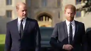 Prinz William und Prinz Harry laufen in schwarzen Anzügen nebeneinander im September 2022