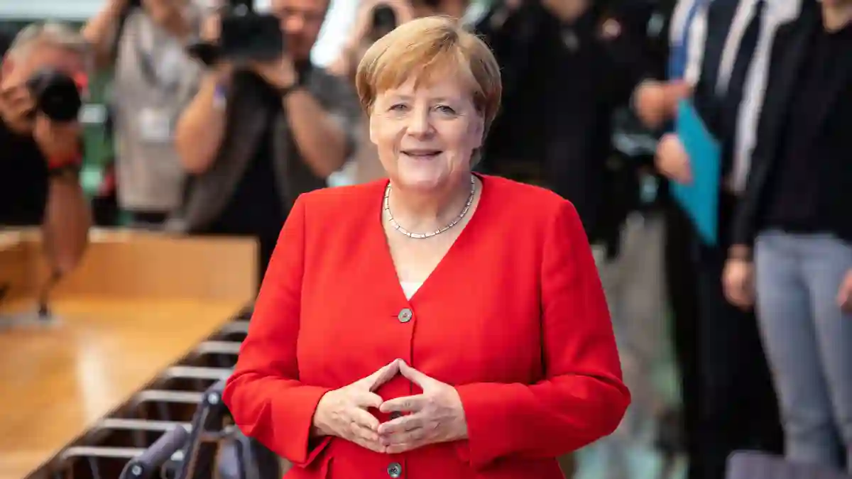 Angela Merkel posiert lächelnd in einem roten Blazer mit der typischen Merkel-Raute bei einem Auftritt im Juli 2019