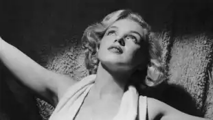 um 1952: Porträt der amerikanischen Schauspielerin Marilyn Monroe (1926 - 1962) in einem tief ausgeschnittenen Neckholder-Top auf einem Teppich.
