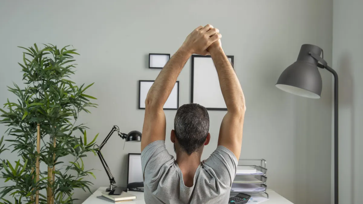 Ein Mann streckt sich am Schreibtisch