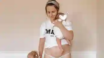 Anna Heiser zeigt ihre Kaiserschnitt-Narbe, während sie ihren Sohn an der Hand und ihre Tochter auf dem Arm hält