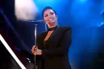 Demi Lovato steht auf der Bühne, lächelt und hält dabei ihr Mikrofon in beiden Händen