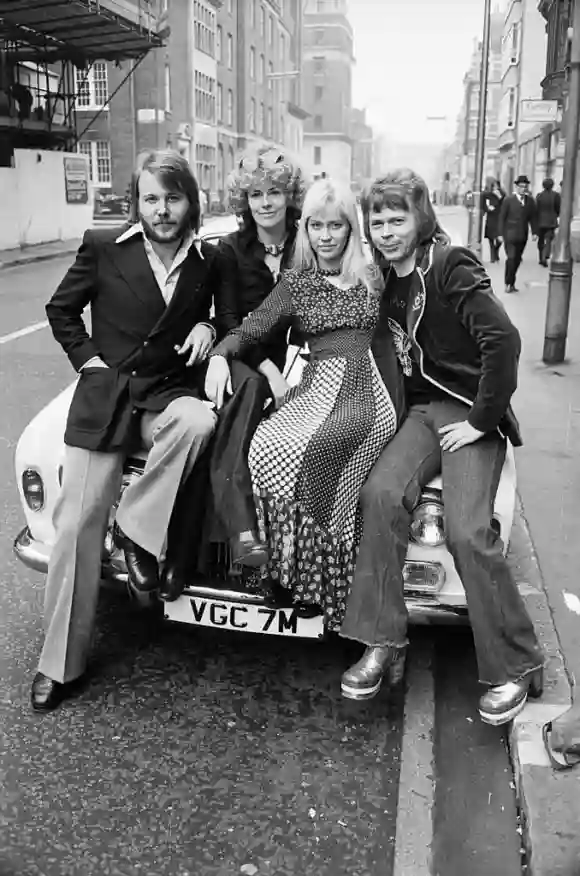 Die Band ABBA posiert an ein Auto gelehnt in einer Straße