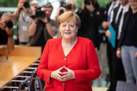 Angela Merkel posiert lächelnd in einem roten Blazer mit der typischen Merkel-Raute bei einem Auftritt im Juli 2019